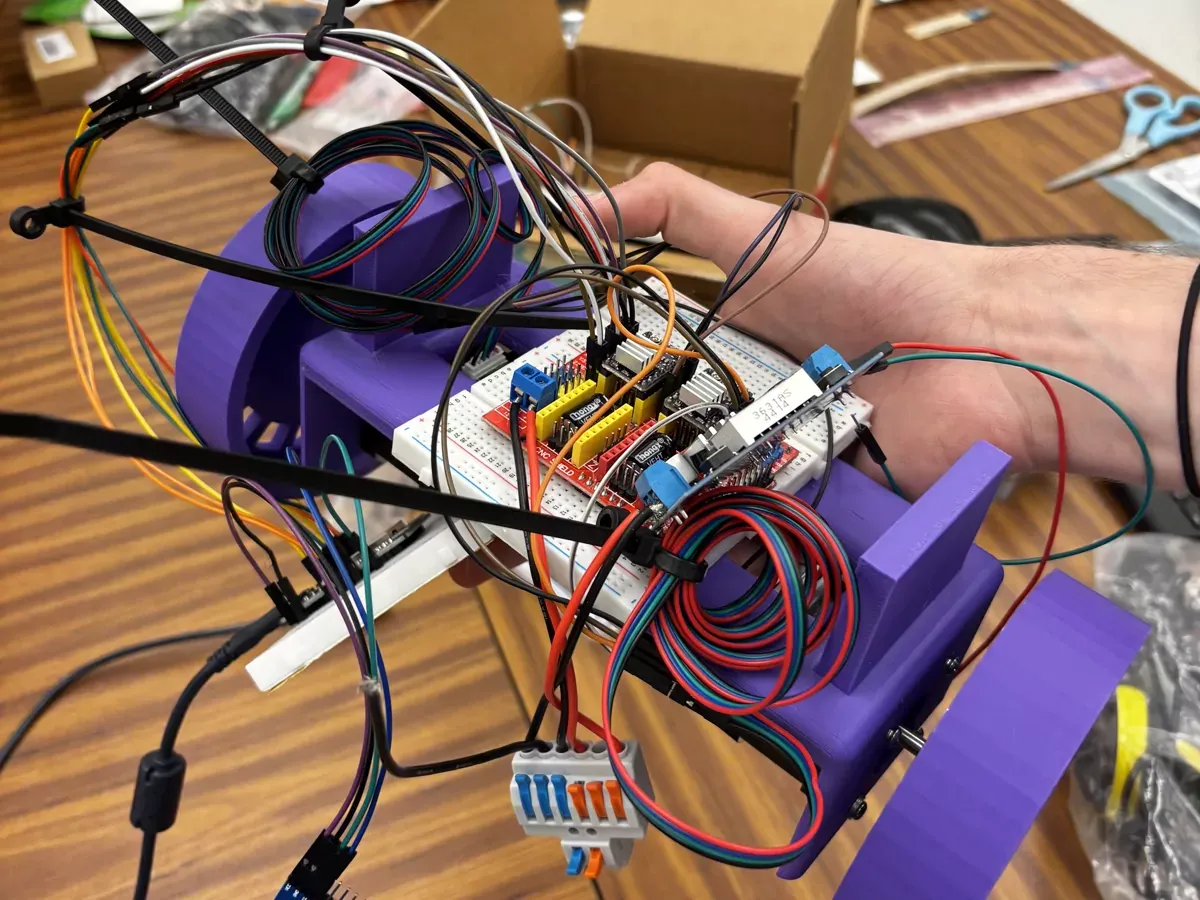 The same prototype held in one hand, showing loops of jumper wire, cable ties and a breadboard packed into the chassis.